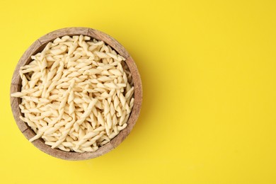 Uncooked trofie pasta in bowl on yellow background, top view. Space for text