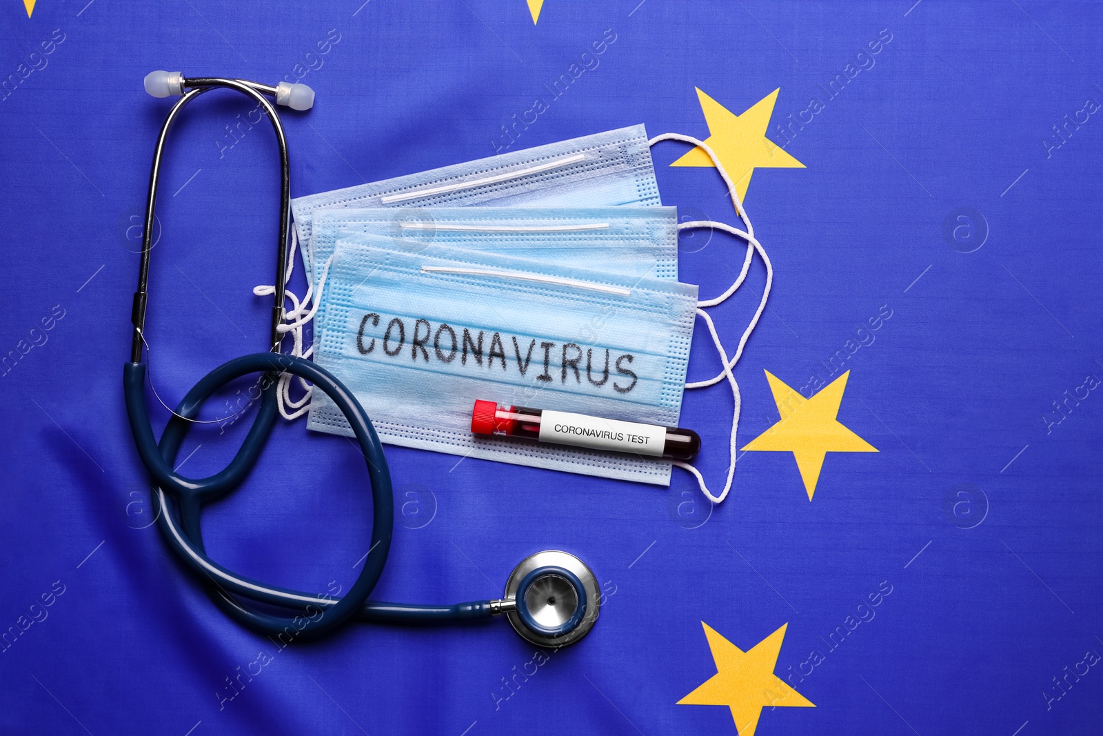 Photo of Stethoscope, protective masks and test tube with blood sample on European Union flag background, flat lay. Coronavirus outbreak