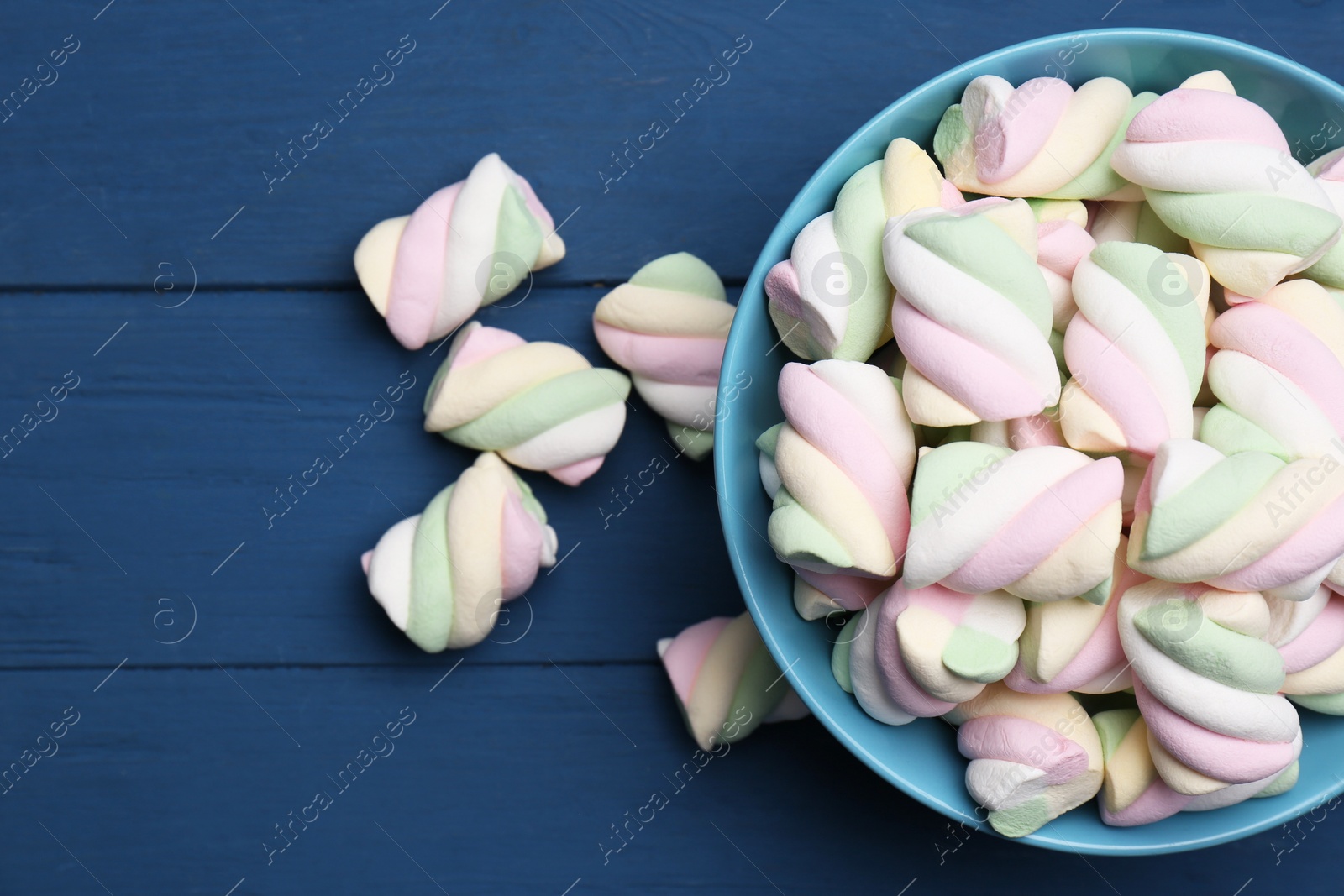 Photo of Bowl with colorful marshmallows on blue wooden table, flat lay. Space for text