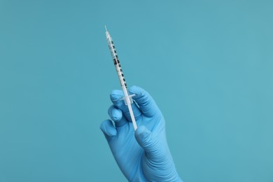 Doctor holding syringe on light blue background, closeup