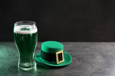 Photo of St. Patrick's day celebration. Green beer with decorative clover leaf and leprechaun hat on grey table. Space for text