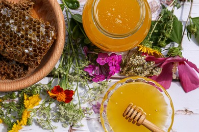 Photo of Delicious honey, combs and different flowers on white wooden table, flat lay