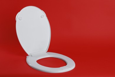 New white plastic toilet seat on red background, space for text