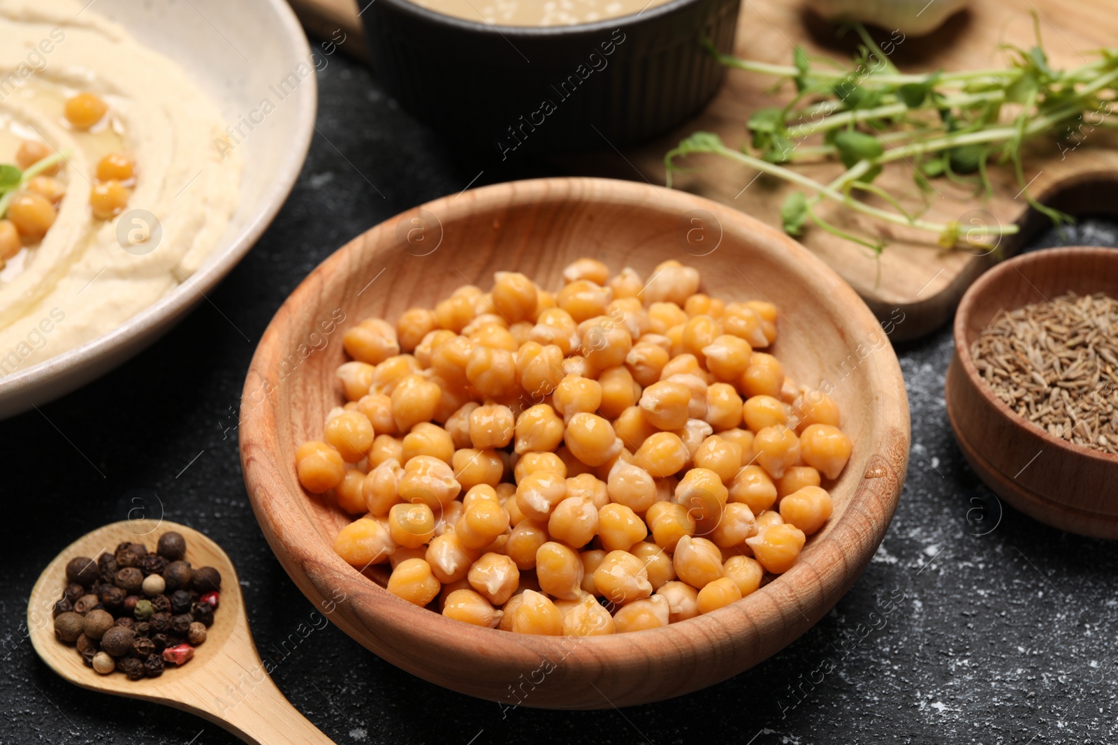 Photo of Delicious chickpeas and different products on black textured table, closeup. Hummus ingredient