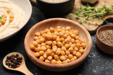 Photo of Delicious chickpeas and different products on black textured table, closeup. Hummus ingredient