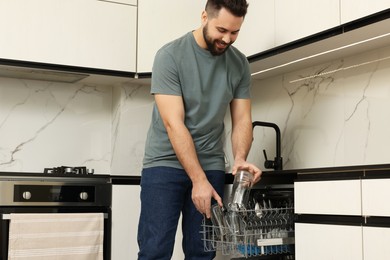Photo of Smiling man loading dishwasher in kitchen, low angle view