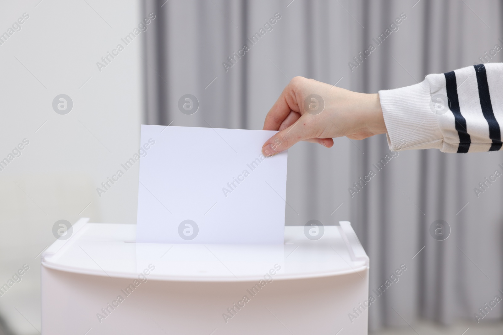 Photo of Woman putting her vote into ballot box on blurred background, closeup