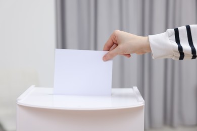 Photo of Woman putting her vote into ballot box on blurred background, closeup