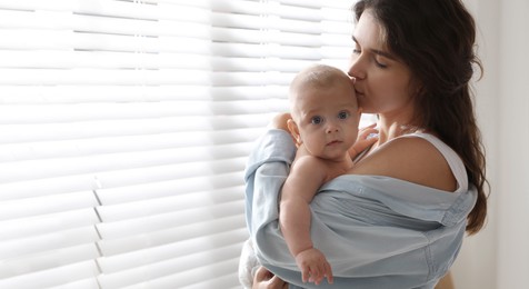 Happy young mother with her cute baby near window at home, space for text. Banner design 