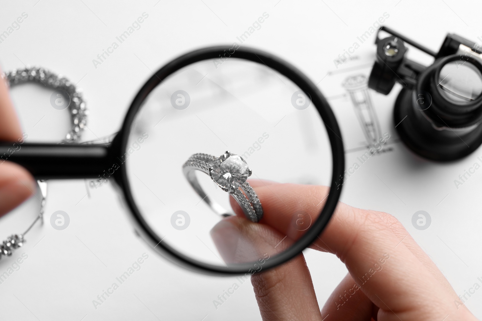 Photo of Jeweler examining diamond ring with magnifying glass at white table, closeup