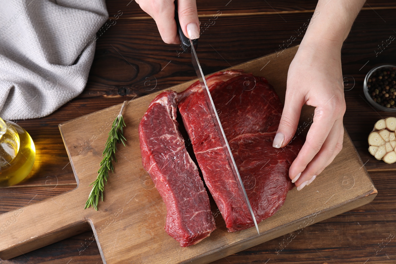 Photo of Woman cutting fresh raw beef steak at wooden table, top view