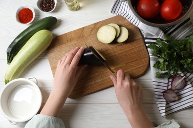 Photo of Cooking delicious ratatouille. Woman cutting fresh eggplant at white wooden table, top view