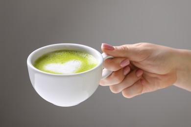 Woman with cup of delicious matcha latte on light grey background, closeup