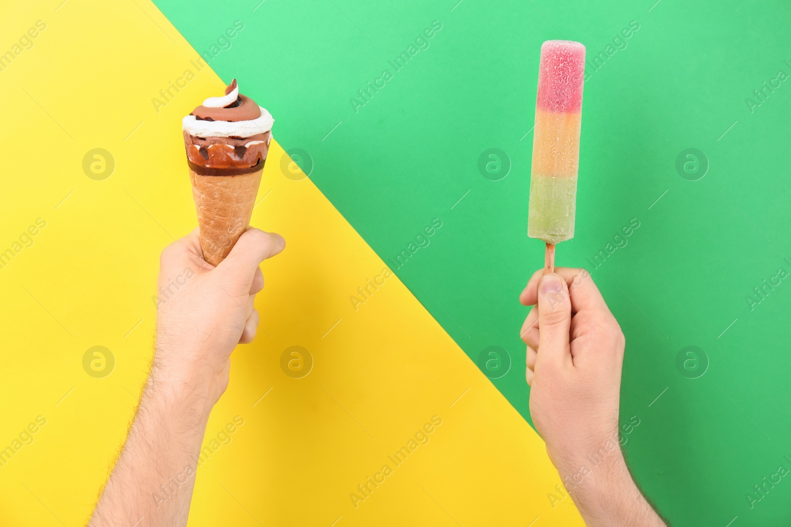 Photo of Man holding ice cream cone and popsicle on color background. Focus on hands