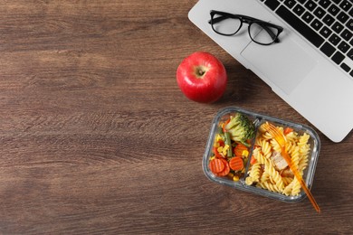Container of tasty food, laptop, apple and glasses on wooden table, flat lay with space for text. Business lunch