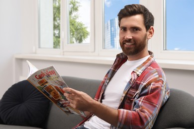 Photo of Smiling bearded man with magazine on sofa indoors