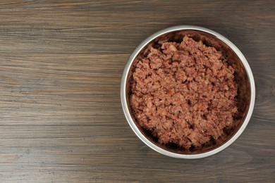 Wet pet food in feeding bowl on wooden background, top view. Space for text