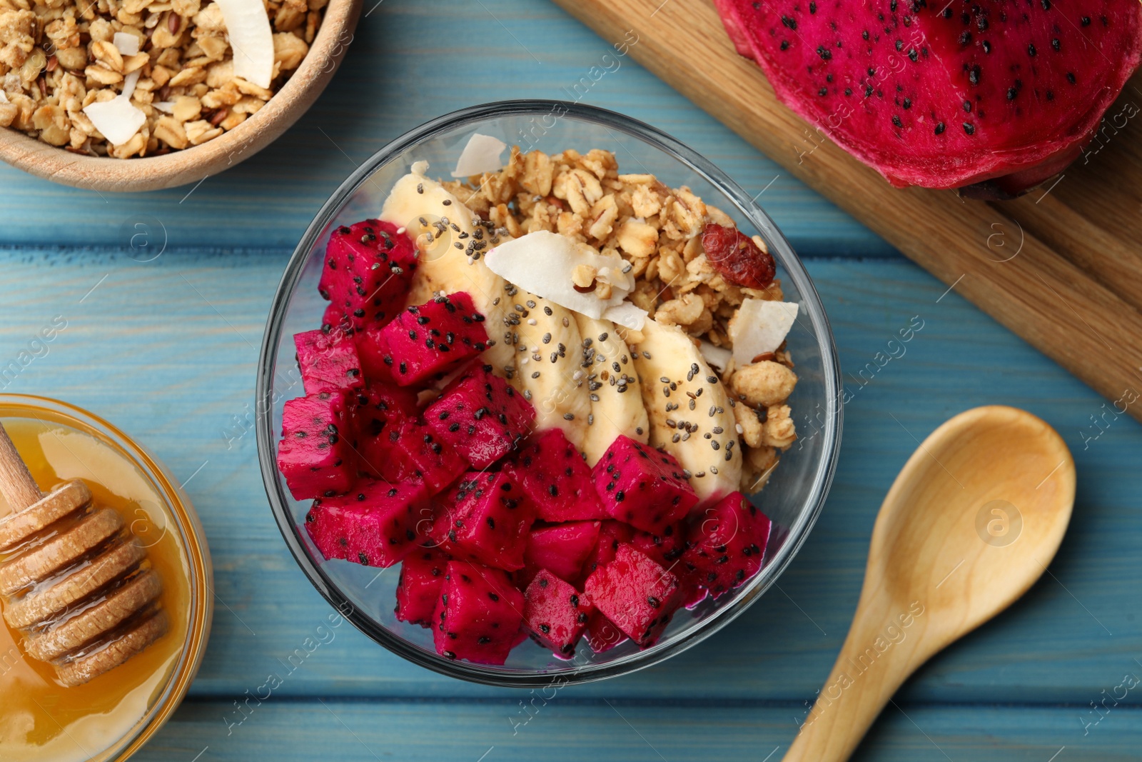 Photo of Bowl of granola with pitahaya and banana served on light blue wooden table, flat lay