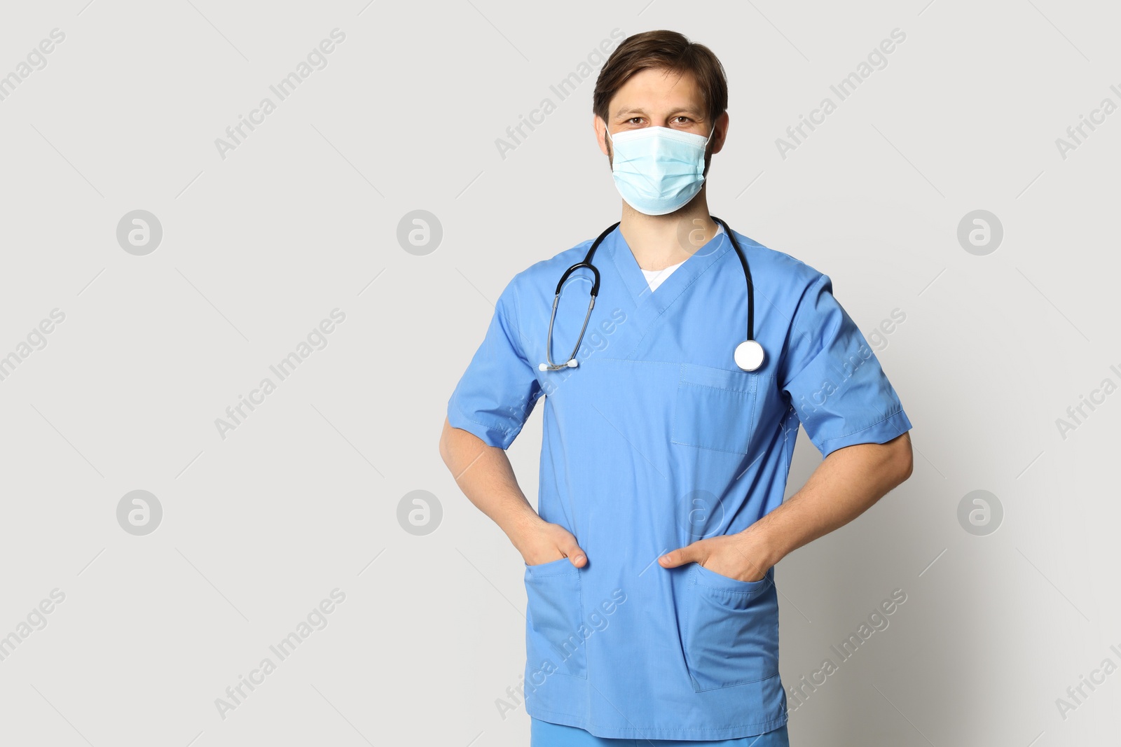 Photo of Doctor or medical assistant (male nurse) with protective mask and stethoscope on light grey background. Space for text