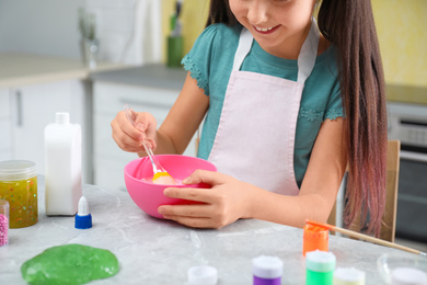 Little girl mixing ingredients with silicone spatula at table in kitchen, closeup. DIY slime toy