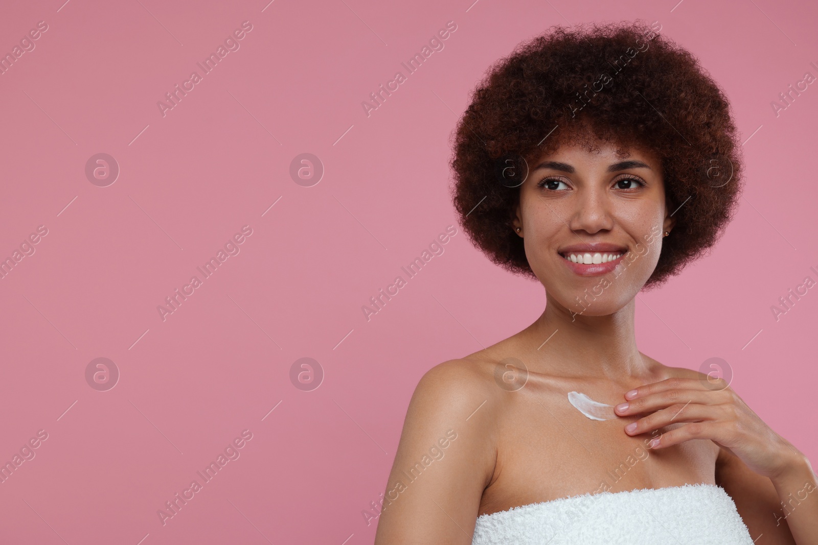 Photo of Beautiful young woman applying cream onto body on pink background, space for text