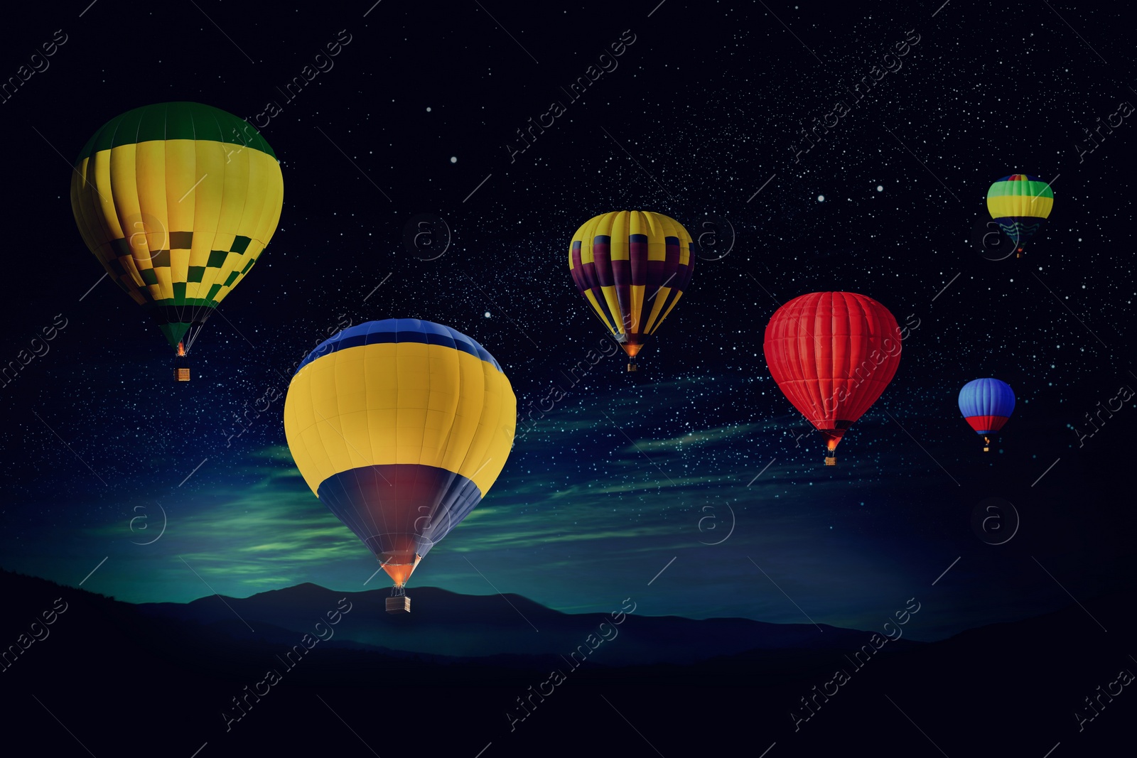 Image of Bright hot air balloons flying in starry sky over mountain at night