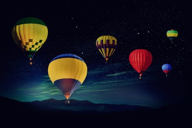 Image of Bright hot air balloons flying in starry sky over mountain at night