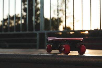 Photo of Modern pink skateboard with red wheels on top of ramp outdoors. Space for text