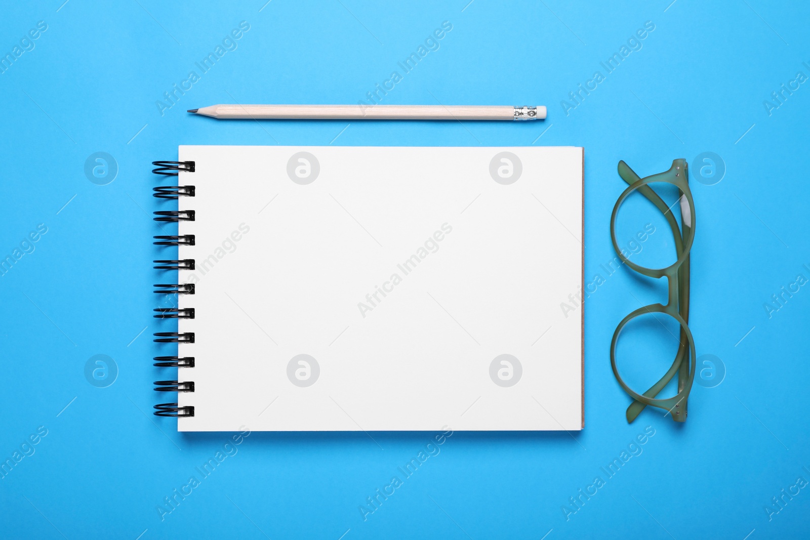 Photo of Open notebook, pencil and glasses on light blue background, flat lay