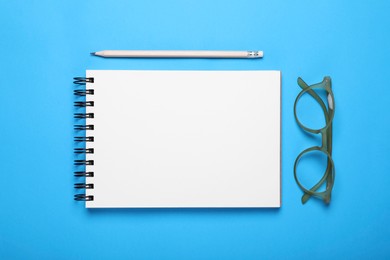 Photo of Open notebook, pencil and glasses on light blue background, flat lay