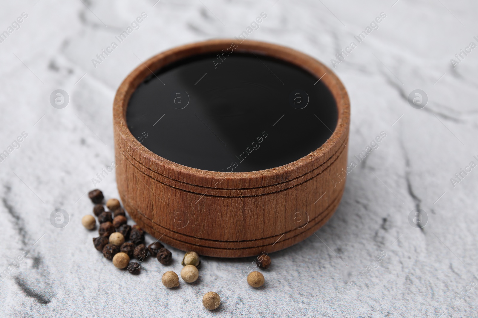 Photo of Wooden bowl with balsamic vinegar and peppercorns on white textured table, closeup