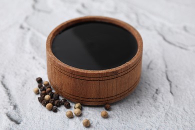 Wooden bowl with balsamic vinegar and peppercorns on white textured table, closeup