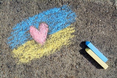Photo of National flag of Ukraine with heart drawn by color chalk and sticks on asphalt, flat lay