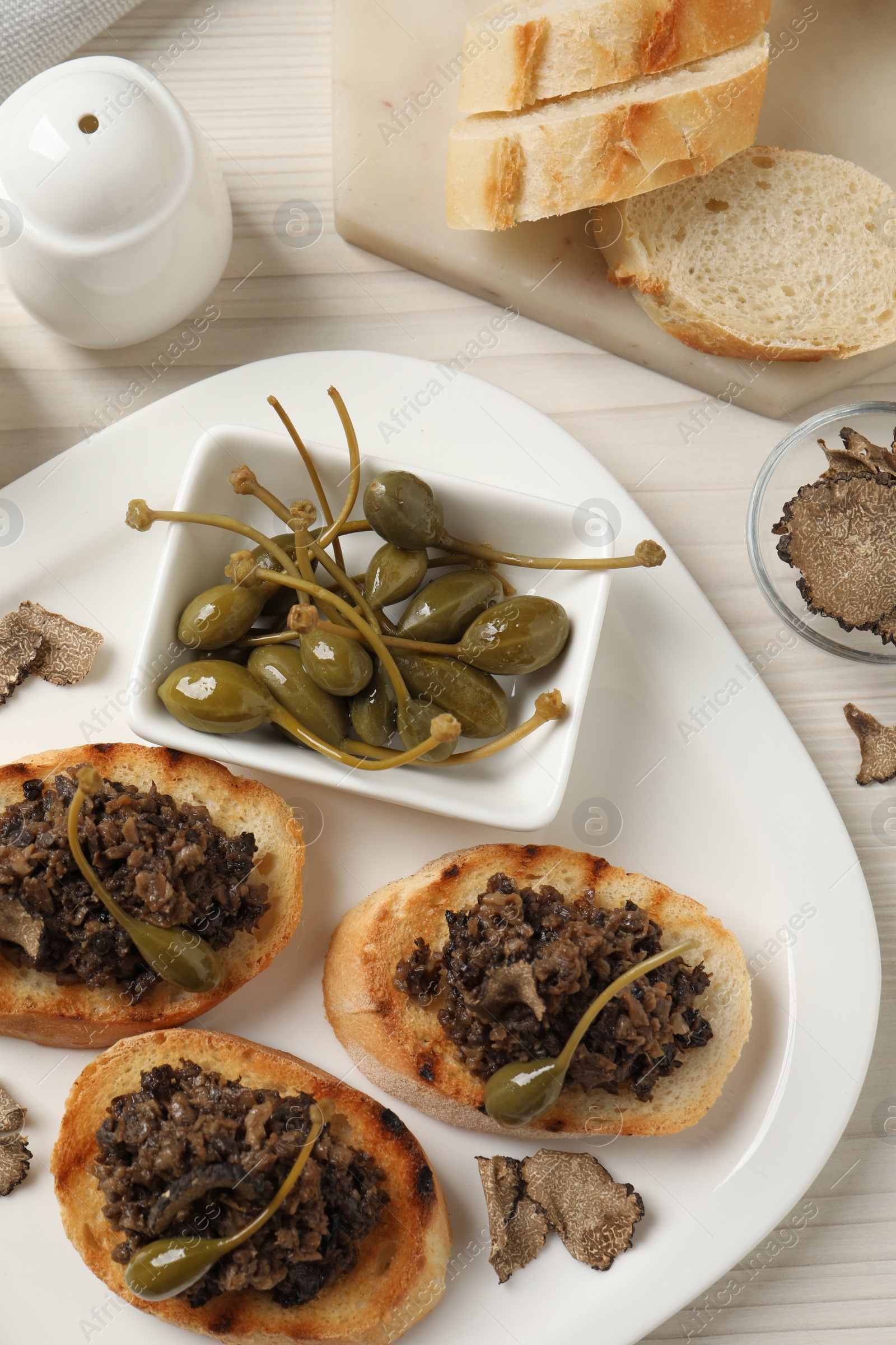 Photo of Delicious bruschettas with truffle sauce and caperberries on white wooden table, flat lay