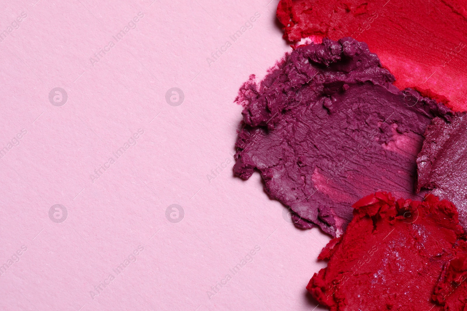 Photo of Smears of beautiful lipsticks on pink background, top view. Space for text