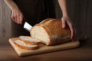 Photo of Woman cutting tasty wheat sodawater bread at wooden table, closeup
