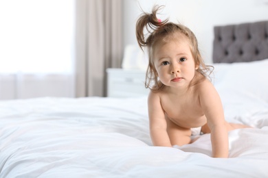 Adorable little baby girl crawling on bed in room. Space for text