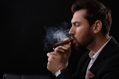 Photo of Handsome man lightning cigar on black background. Space for text