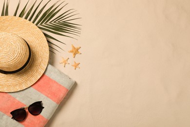 Beach towel, sunglasses, hat, palm leaf and starfishes on sand, flat lay. Space for text