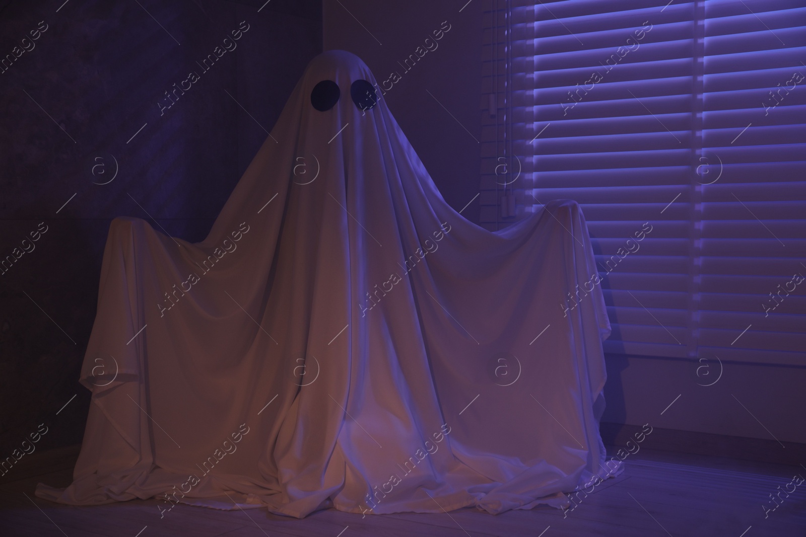 Photo of Creepy ghost. Woman covered with sheet near window in color lights