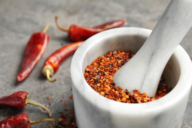 Photo of Mortar with crushed chili pepper on grey background, closeup