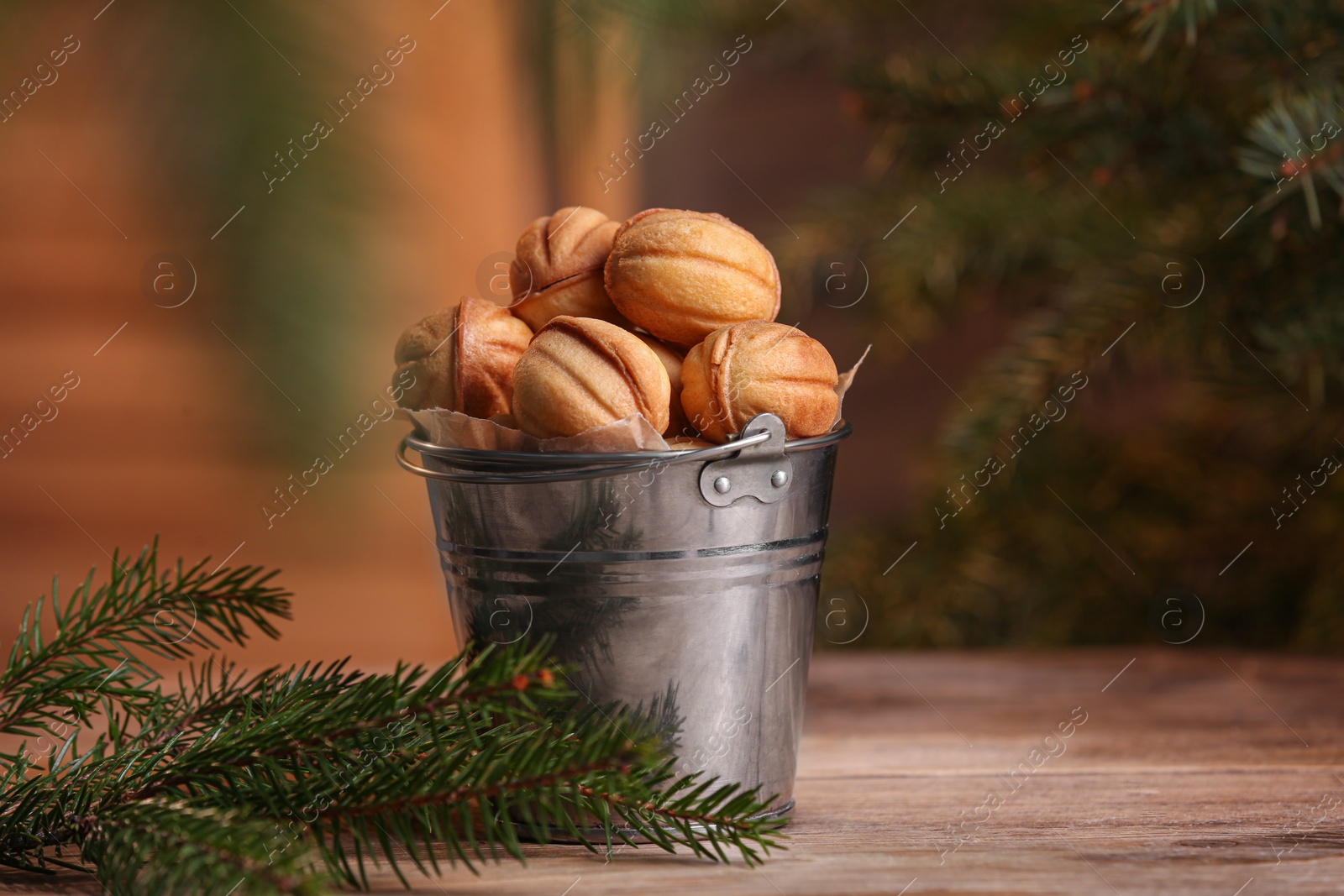 Photo of Metal bucket of delicious nut shaped cookies and fir branches on wooden table, space for text