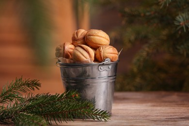 Metal bucket of delicious nut shaped cookies and fir branches on wooden table, space for text