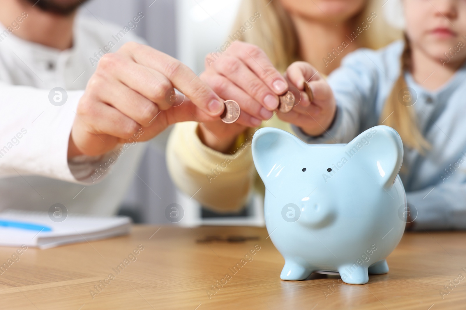 Photo of Planning budget together. Little girl with her family putting coins into piggybank at table, closeup