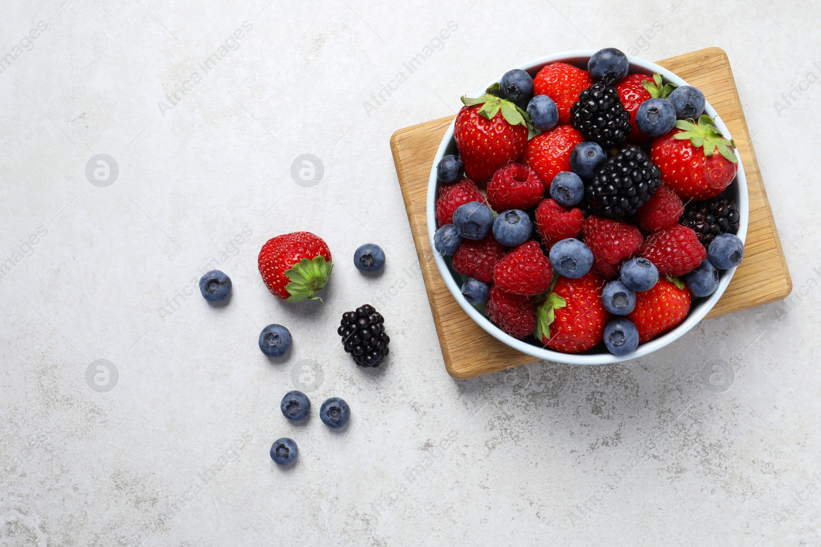 Photo of Many different fresh ripe berries in bowl on light grey table, flat lay. Space for text