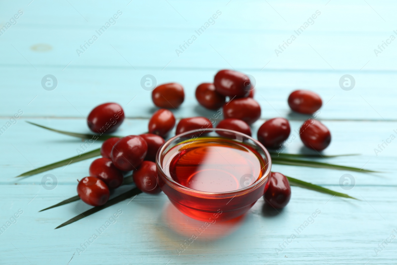 Photo of Palm oil in glass bowl, tropical leaf and fruits on light blue wooden table