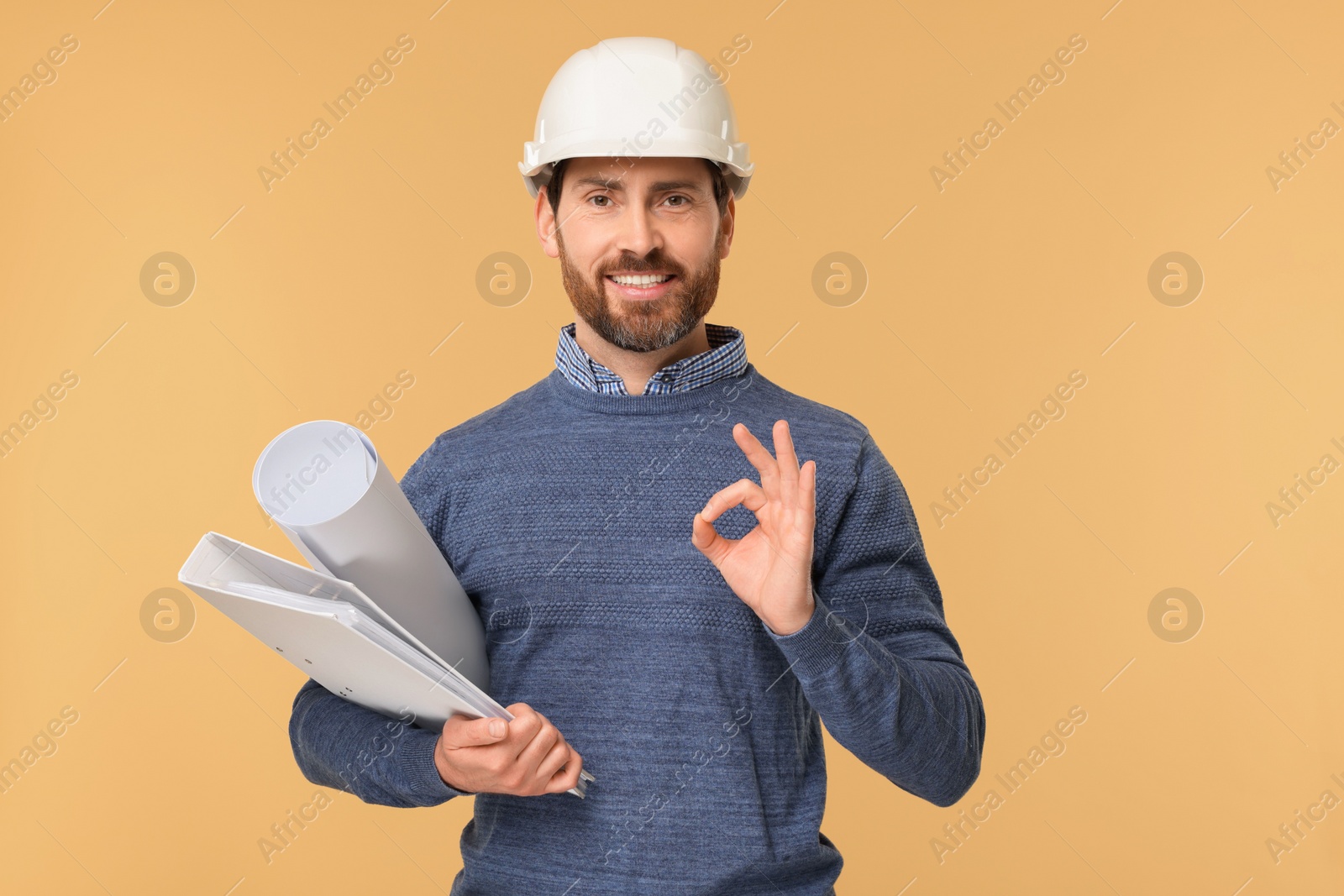 Photo of Architect in hard hat with draft and folder showing OK gesture on beige background