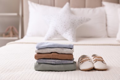 Stack of baby boy's clothes and shoes on bed at home, space for text