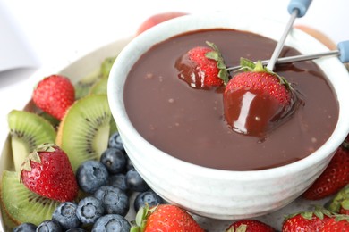 Photo of Dipping strawberries into fondue pot with chocolate, closeup