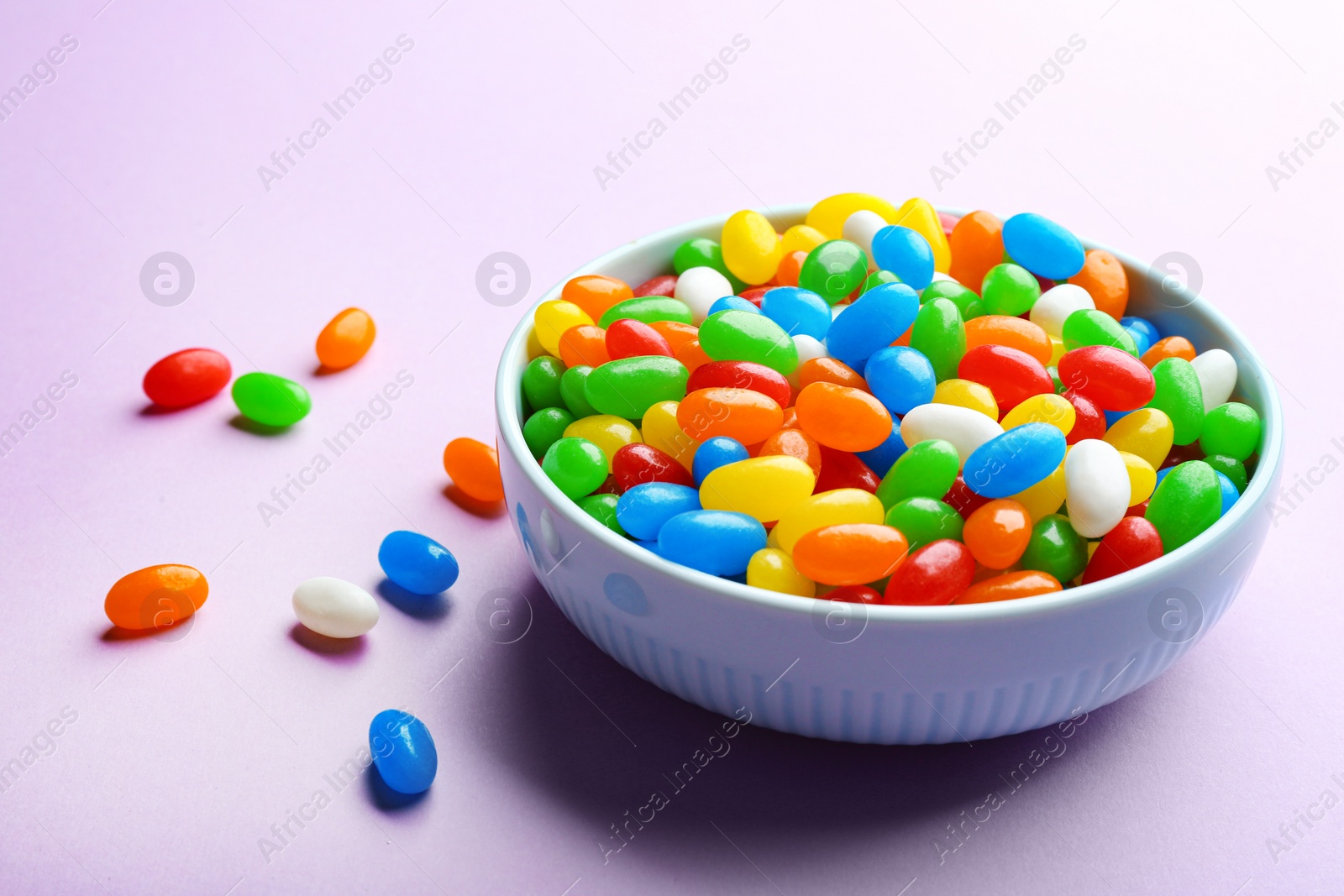 Photo of Bowl with colorful jelly beans on lilac background. Space for text